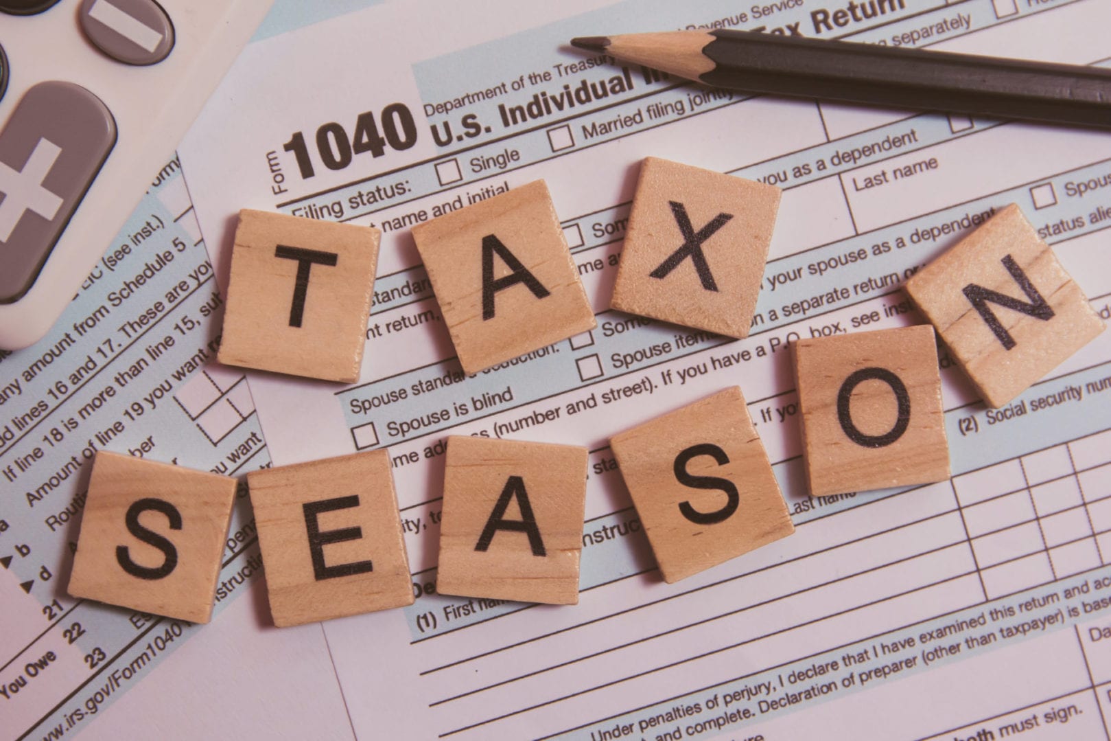 Tax season with wooden alphabet blocks, calculator, pencil on 1040 tax form background
